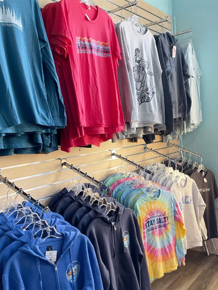 Rack of Coos Bay Oregon tees, a seahorse graphic shirt, hoodies, and a Stay Salty tie dye shirt