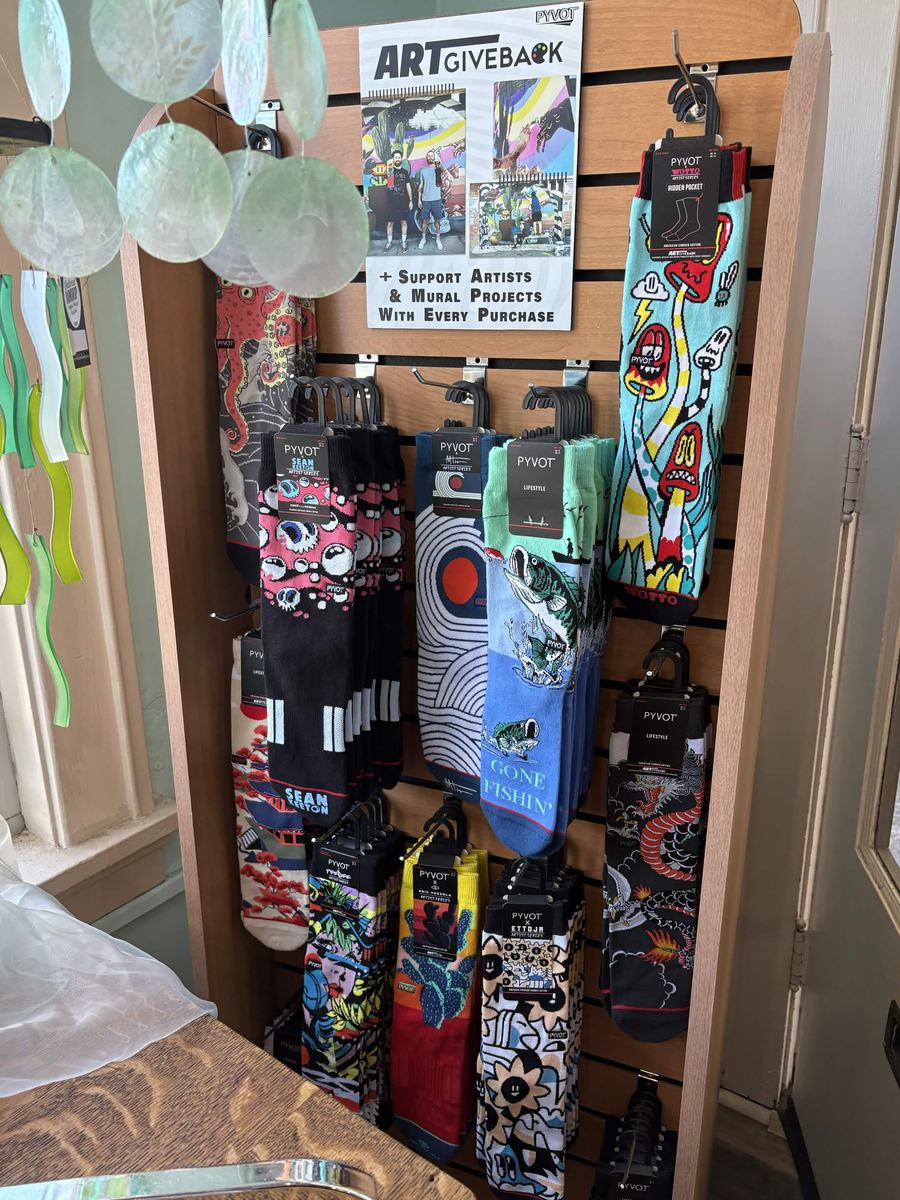 Rack of colorful artist series socks under an Art Giveback sign supporting artists and murals