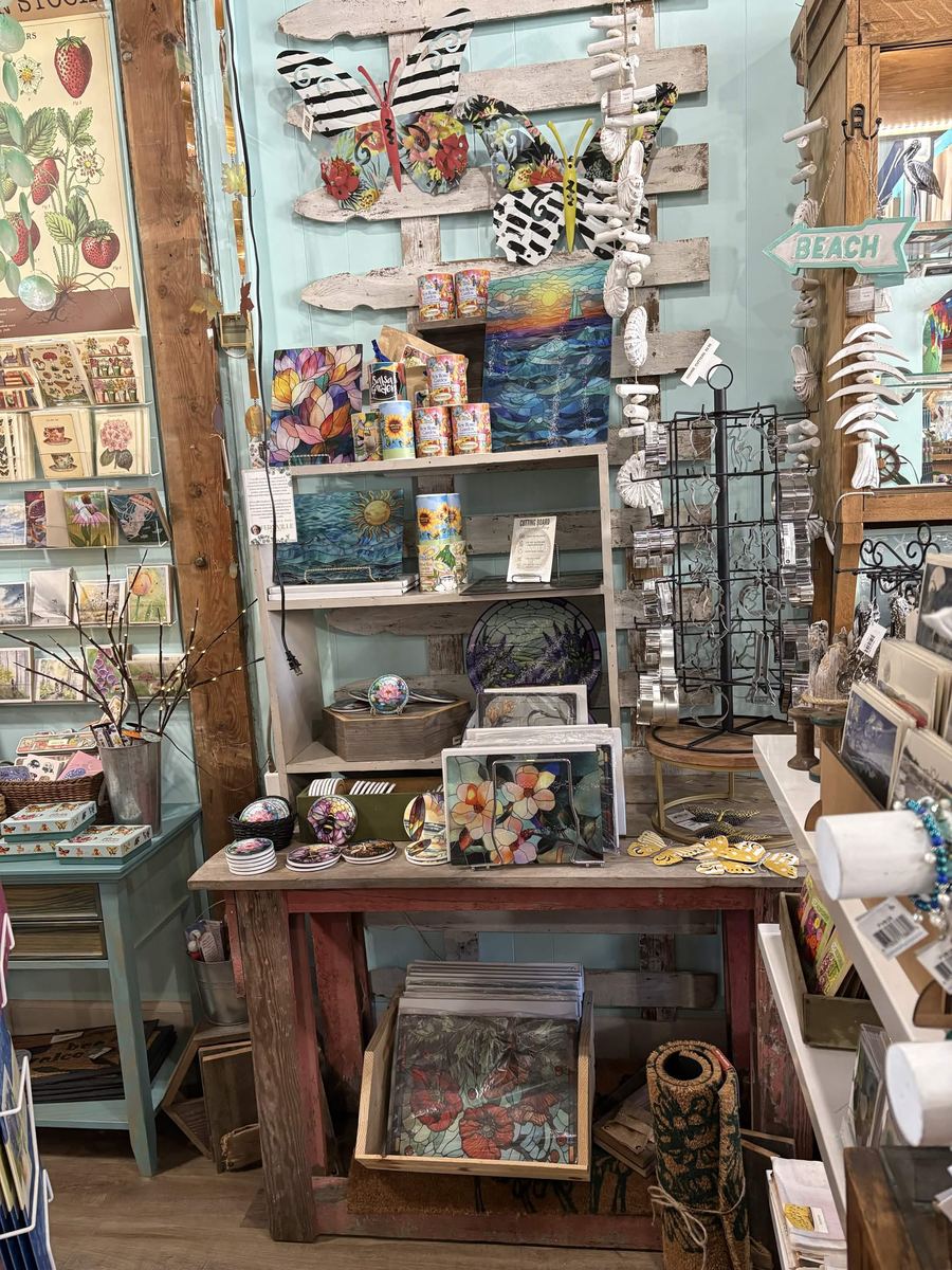 Wall of greeting cards, stained glass art, and a coastal beach sign inside Bayshore Gifts and Gallery