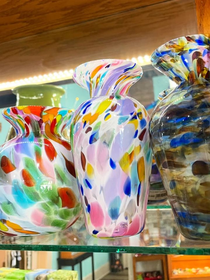 Three hand blown art glass vases with colorful confetti speckles on a glass shelf